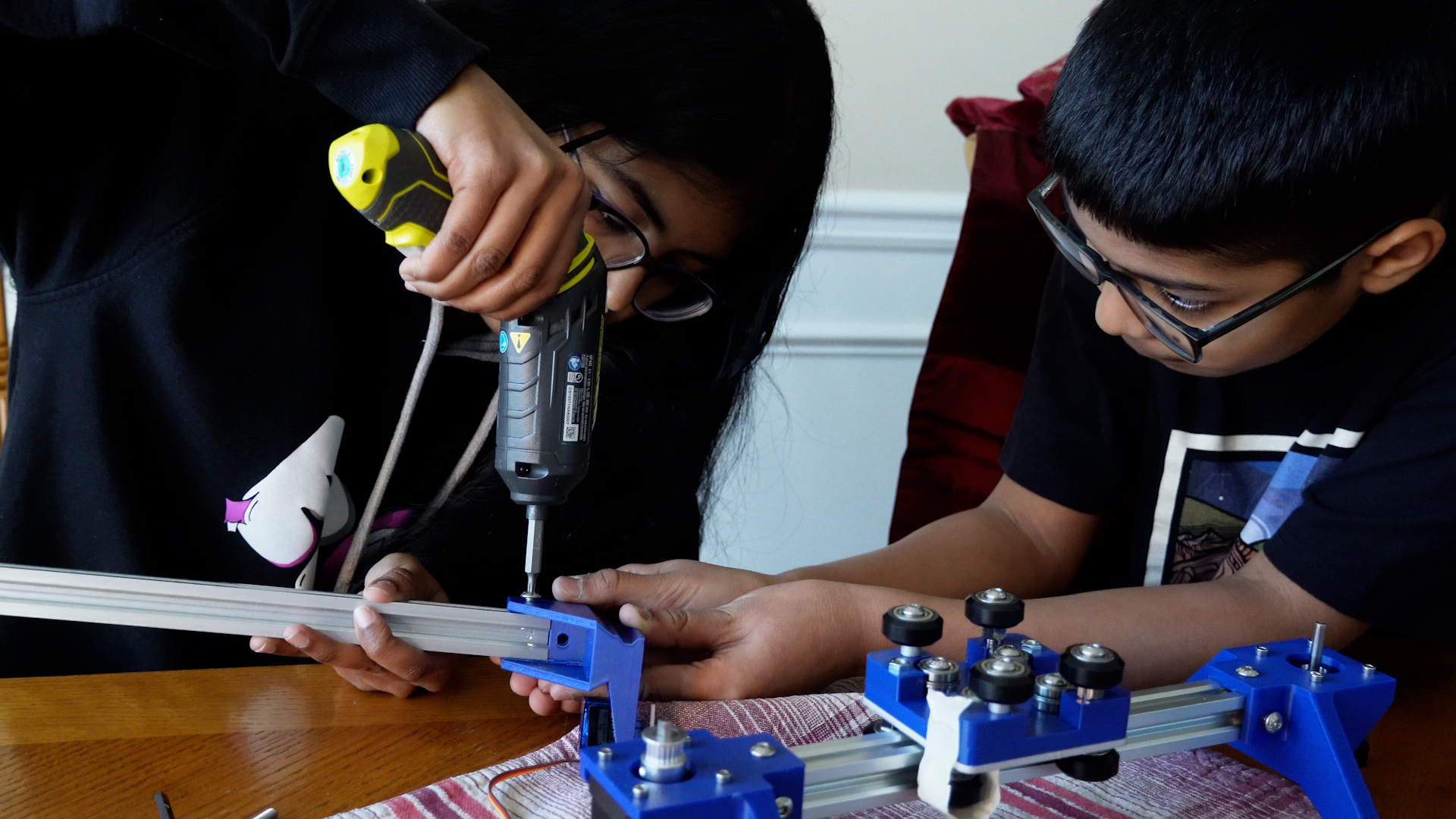 Two kids putting together a blot machine with an electric screwdriver.